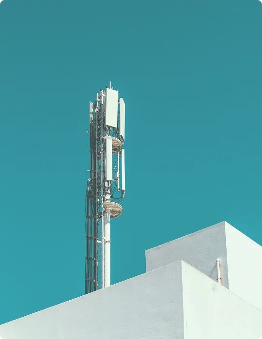 Cell tower on white building against blue sky.