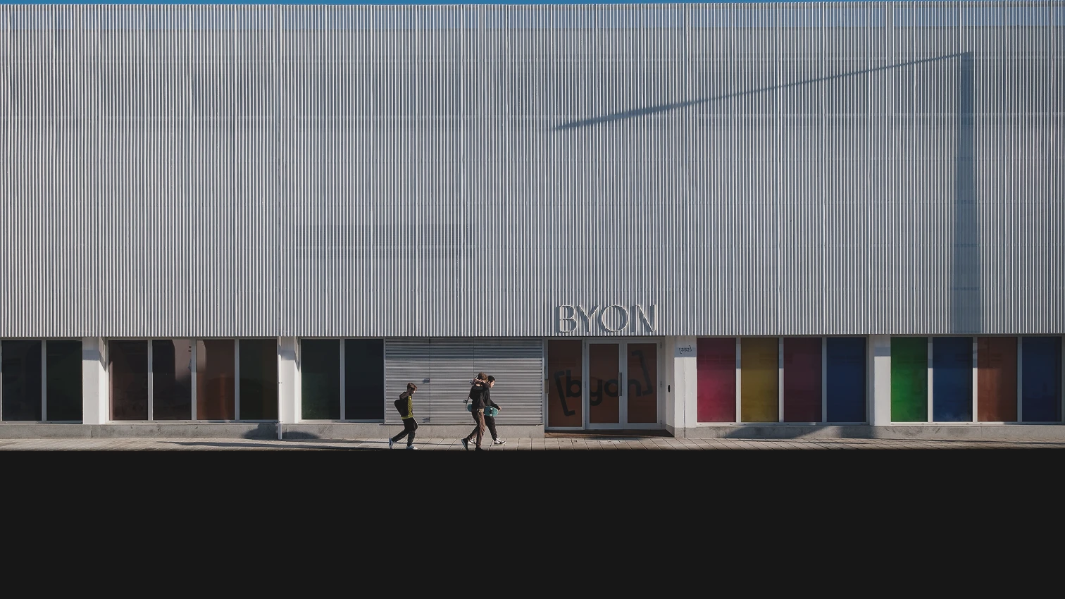 People walking by a modern building with colorful windows.