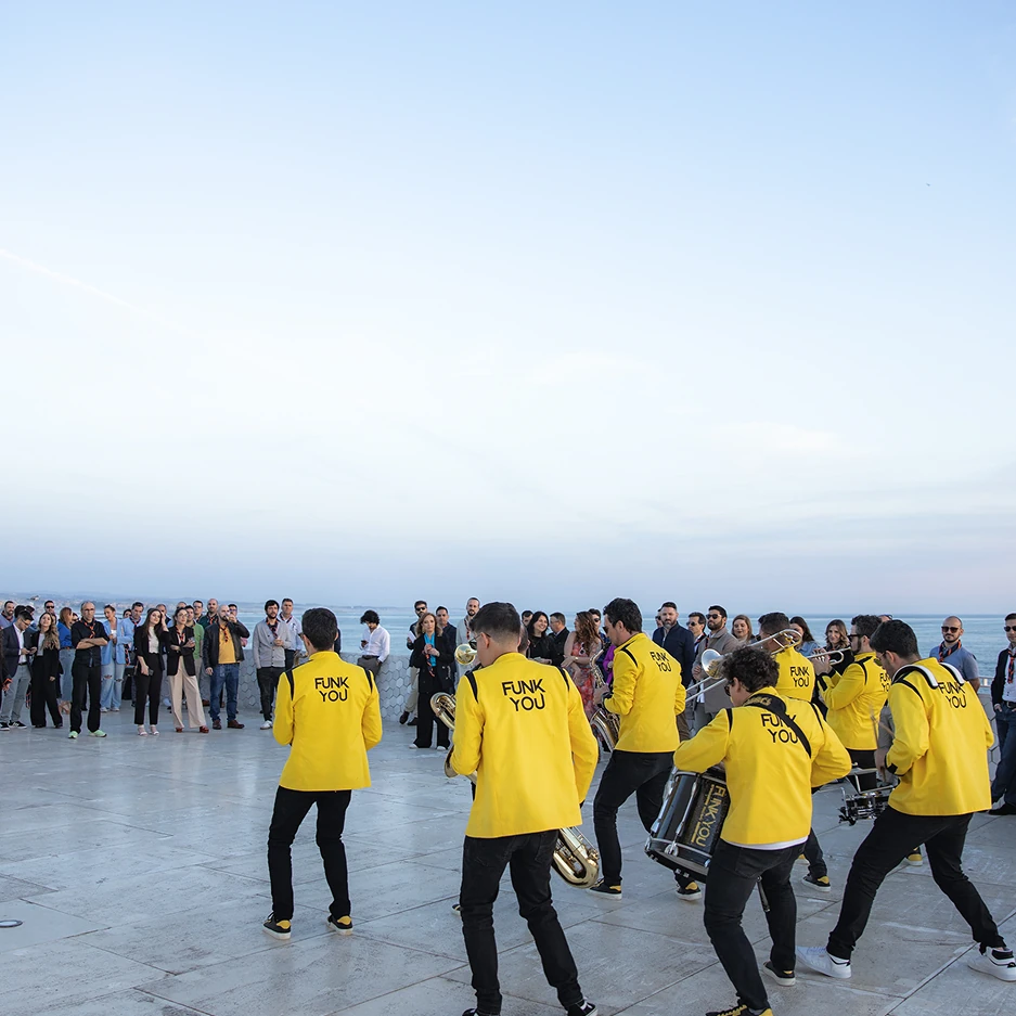 Band performing outdoors to crowd, wearing yellow jackets.